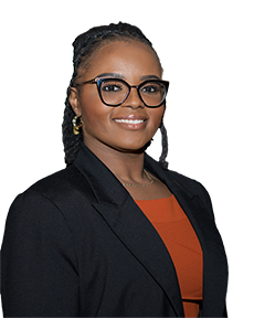 Smiling woman with glasses wearing a black blazer and orange top in an indoor setting.