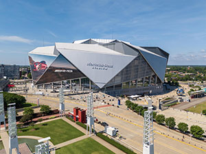 Aerial view of Mercedes-Benz Stadium with its distinctive angular, retractable roof partially open under a blue sky.